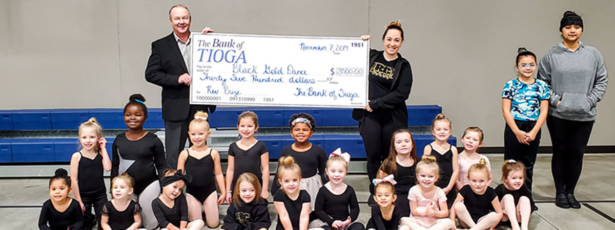 employee and dancers pose with large check